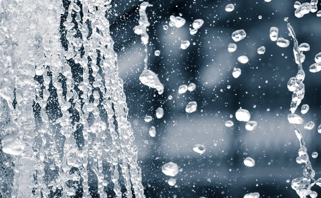 Vandstråler og vanddråber i bevægelse, brugt til at illustrere måling af vands hårdhed og forskellen mellem blødt og hårdt vand.